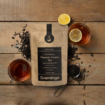 a pouch of premium loose black tea from Sri Lanka laying on the floor with two freshly-made tea cups full of rich aroma and color