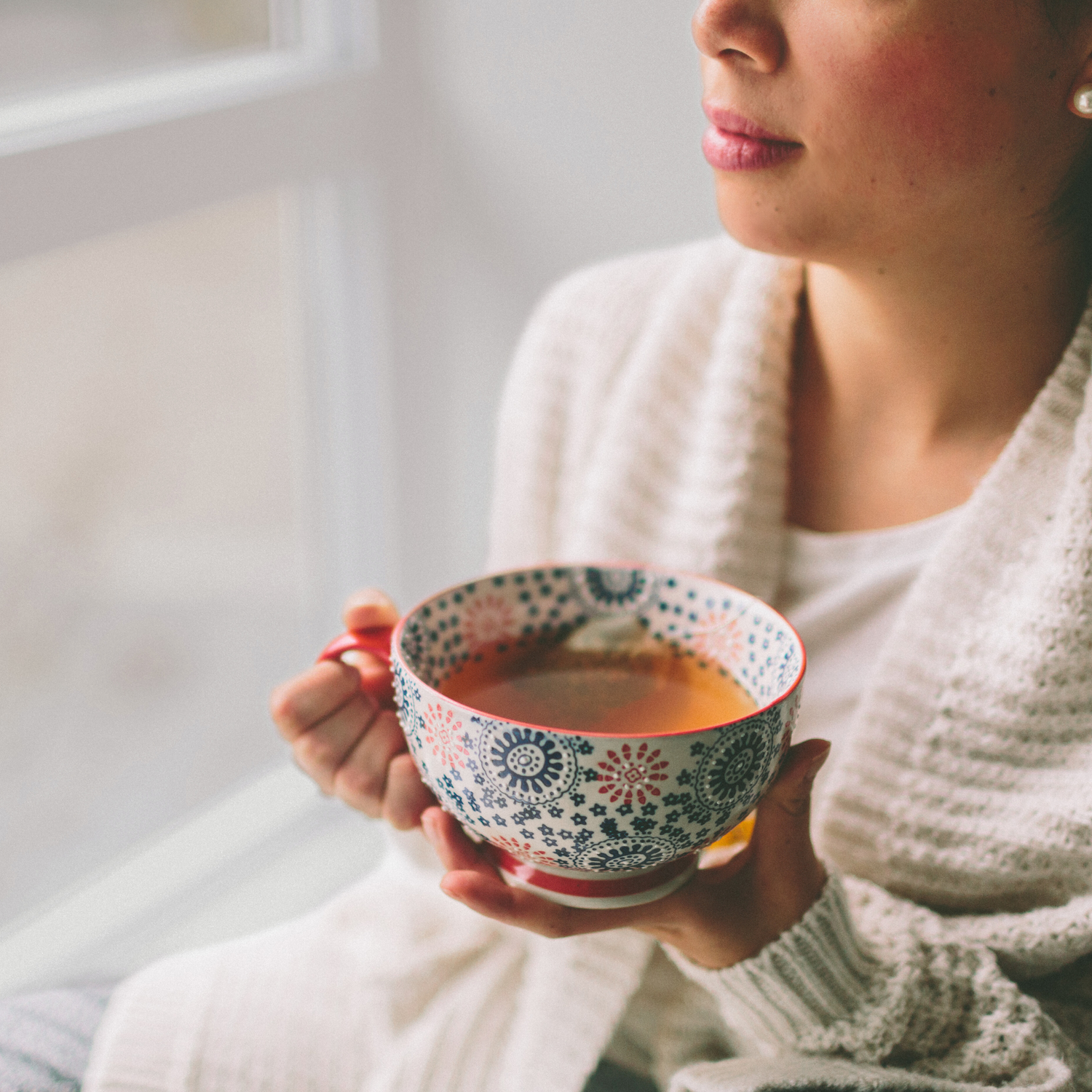 A woman holding a tea cup enjoying her daily tea ritual and looking across the window